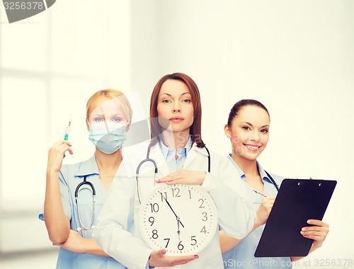 Image of calm female doctor and nurses with wall clock