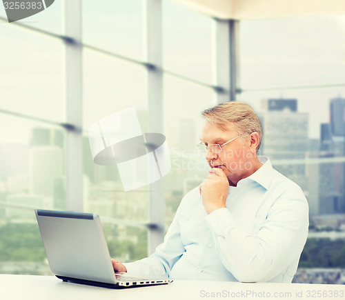 Image of senior man in eyeglasses with laptop at office