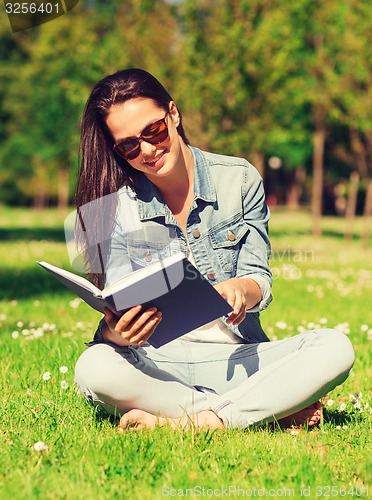 Image of smiling young girl with book sitting in park