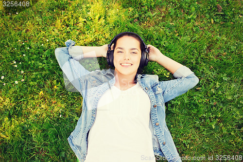 Image of smiling young girl in headphones lying on grass