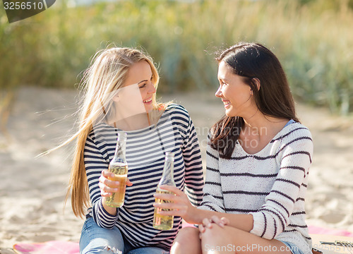 Image of happy young women drinking beer on beach