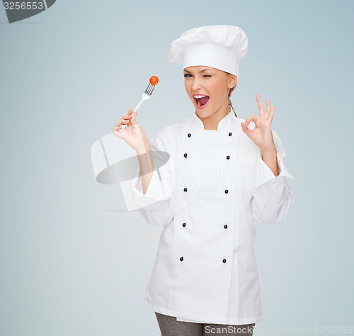 Image of smiling female chef with fork and tomato