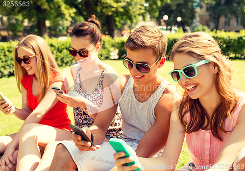 Image of smiling friends with smartphones sitting on grass