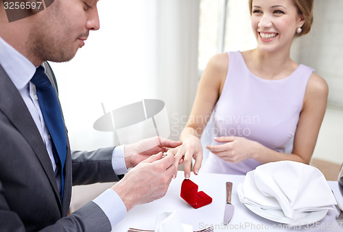 Image of close up of man putting ring to his fiance finger