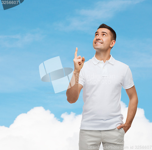 Image of smiling man pointing finger up over blue sky
