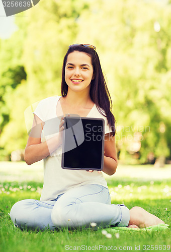 Image of smiling young girl with tablet pc sitting on grass