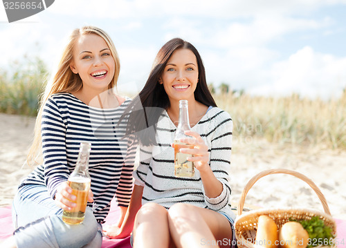 Image of happy young women drinking beer on beach