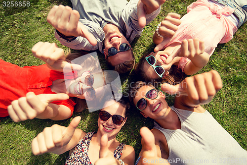 Image of smiling friends showing thumbs up lying on grass