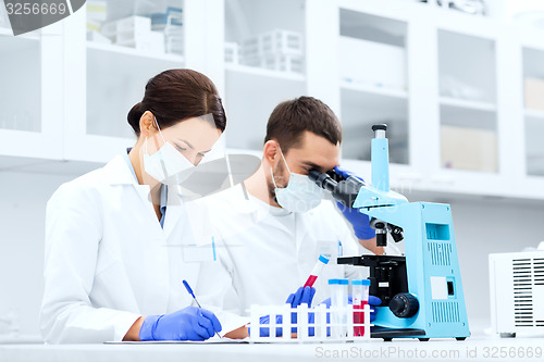 Image of scientists with clipboard and microscope in lab