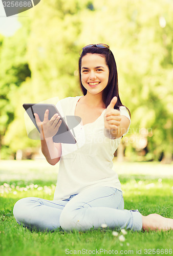 Image of smiling young girl with tablet pc sitting on grass