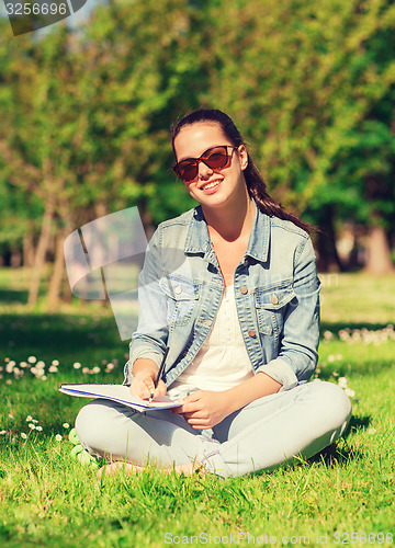 Image of smiling young girl with notebook writing in park