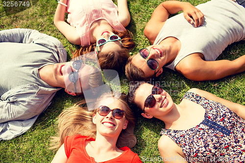 Image of group of smiling friends lying on grass outdoors