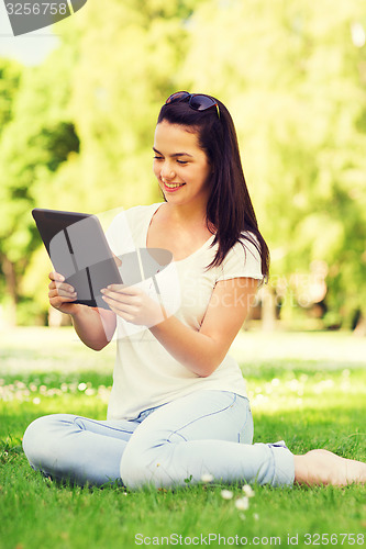 Image of smiling young girl with tablet pc sitting on grass
