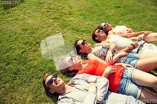 Image of group of smiling friends lying on grass outdoors