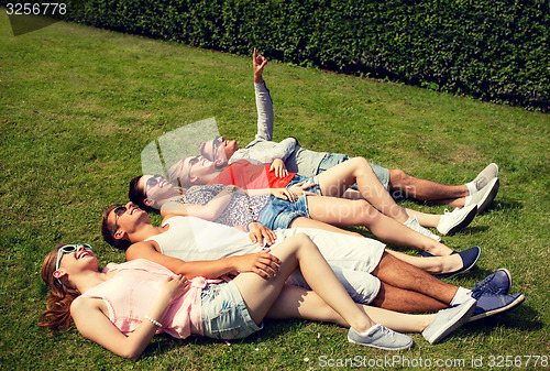 Image of group of smiling friends lying on grass outdoors