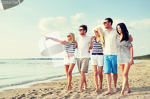 Image of smiling friends in sunglasses walking on beach