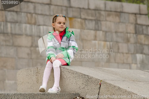 Image of girl looks into distance while sitting a granite embankment on ramp