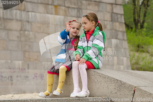 Image of Girl shows something other girl, sitting on a granite ramp