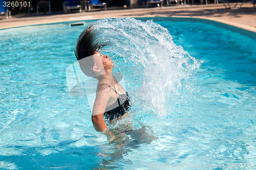 Image of Pretty teen girl whipping her hair back in the pool and spraying water everywhere