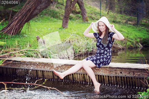 Image of Cheerful fashionable woman sits on small bridge and splashing wa