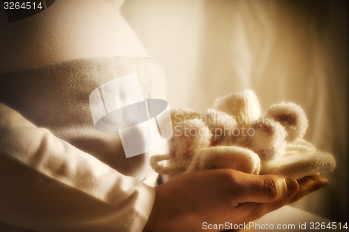 Image of Pregnant woman is holding baby shoes