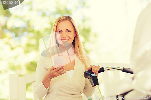 Image of happy mother with smartphone and stroller in park