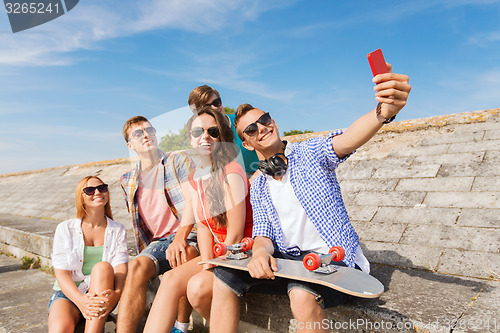 Image of group of smiling friends with smartphone outdoors