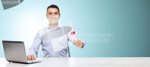 Image of smiling man with diploma and laptop at table