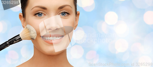 Image of happy woman applying powder foundation with brush