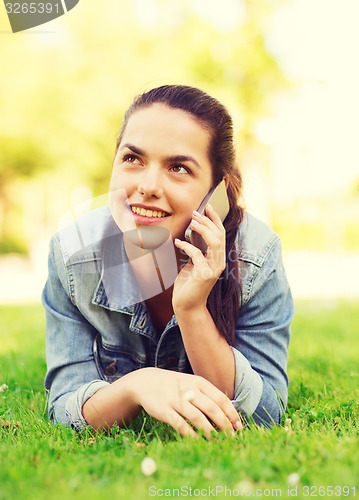 Image of smiling young girl with smartphone lying on grass