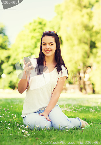 Image of smiling young girl with smartphone sitting in park