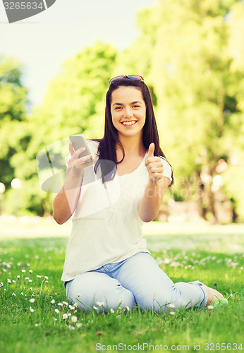 Image of smiling young girl with smartphone sitting in park