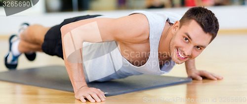 Image of smiling man doing push-ups in the gym