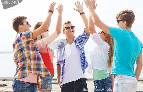 Image of group of smiling friends making high five outdoors