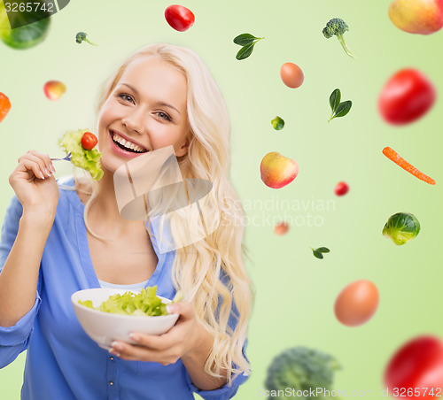 Image of smiling young woman eating green vegetable salad