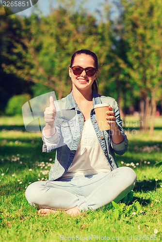 Image of smiling young girl with cup of coffee in park