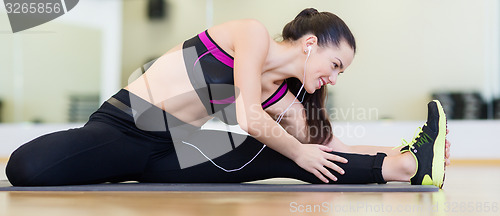 Image of smiling girl with earphones stretching on mat