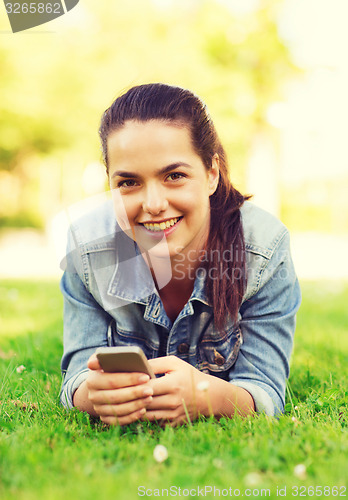 Image of smiling young girl with smartphone lying on grass