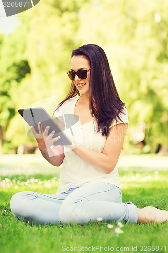 Image of smiling young girl with tablet pc sitting on grass