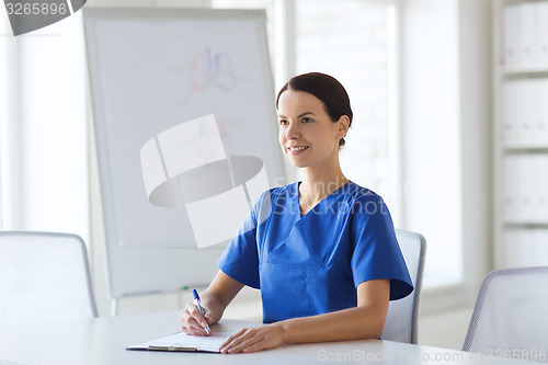 Image of happy female doctor or nurse writing to clipboard