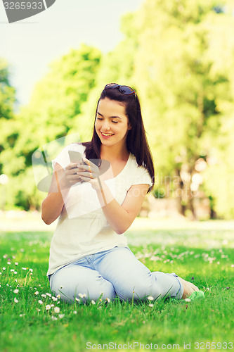 Image of smiling young girl with smartphone sitting in park