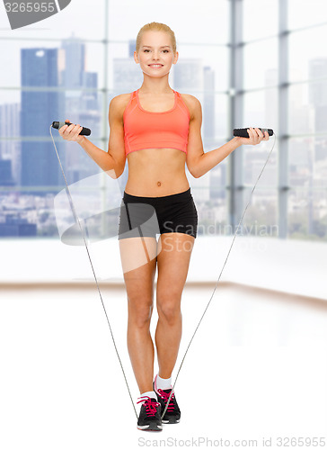 Image of smiling sporty woman jumping  with skipping rope