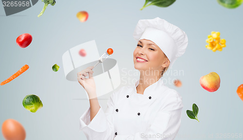 Image of smiling female chef with fork and tomato