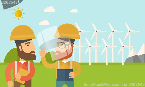 Image of Two workers talking infront of windmills.