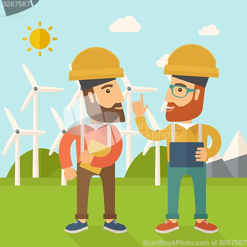 Image of Two workers talking infront of windmills.