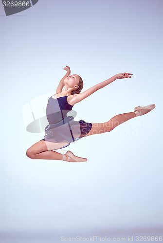 Image of Beautiful young ballet dancer jumping on a gray background. 