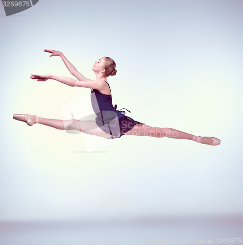 Image of Beautiful young ballet dancer jumping on a gray background. 