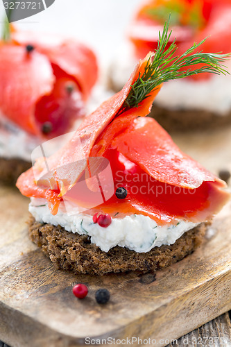 Image of Sandwich of black bread, cheese with herbs and red salmon.