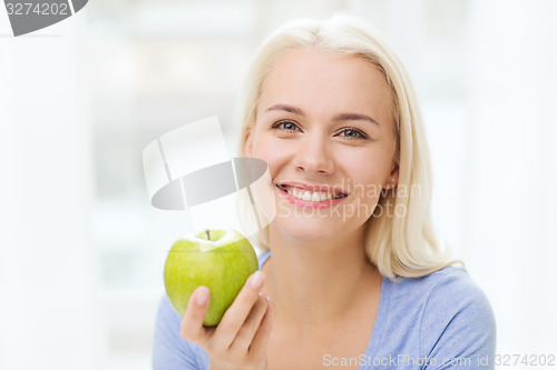 Image of happy woman eating green apple at home