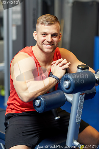Image of smiling man sitting on exercise bench in gym
